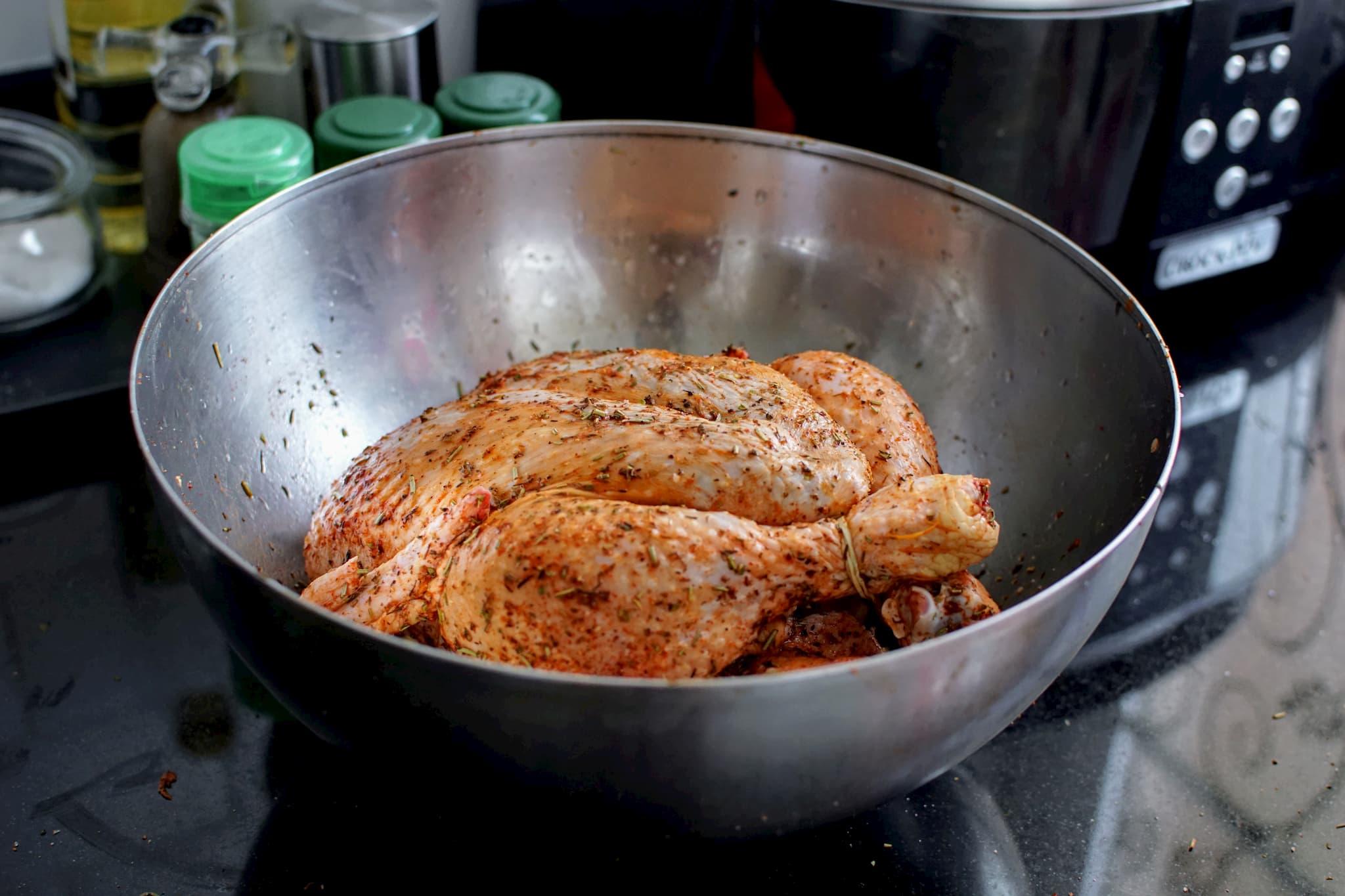 Fresh whole chicken rubbed with spices and aromatic herbs in a big stainless steel bowl