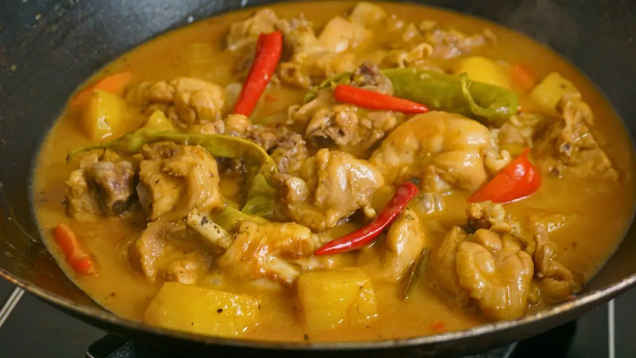 Chicken curry simmering in coconut milk with potatoes, carrots, and long green chilies
