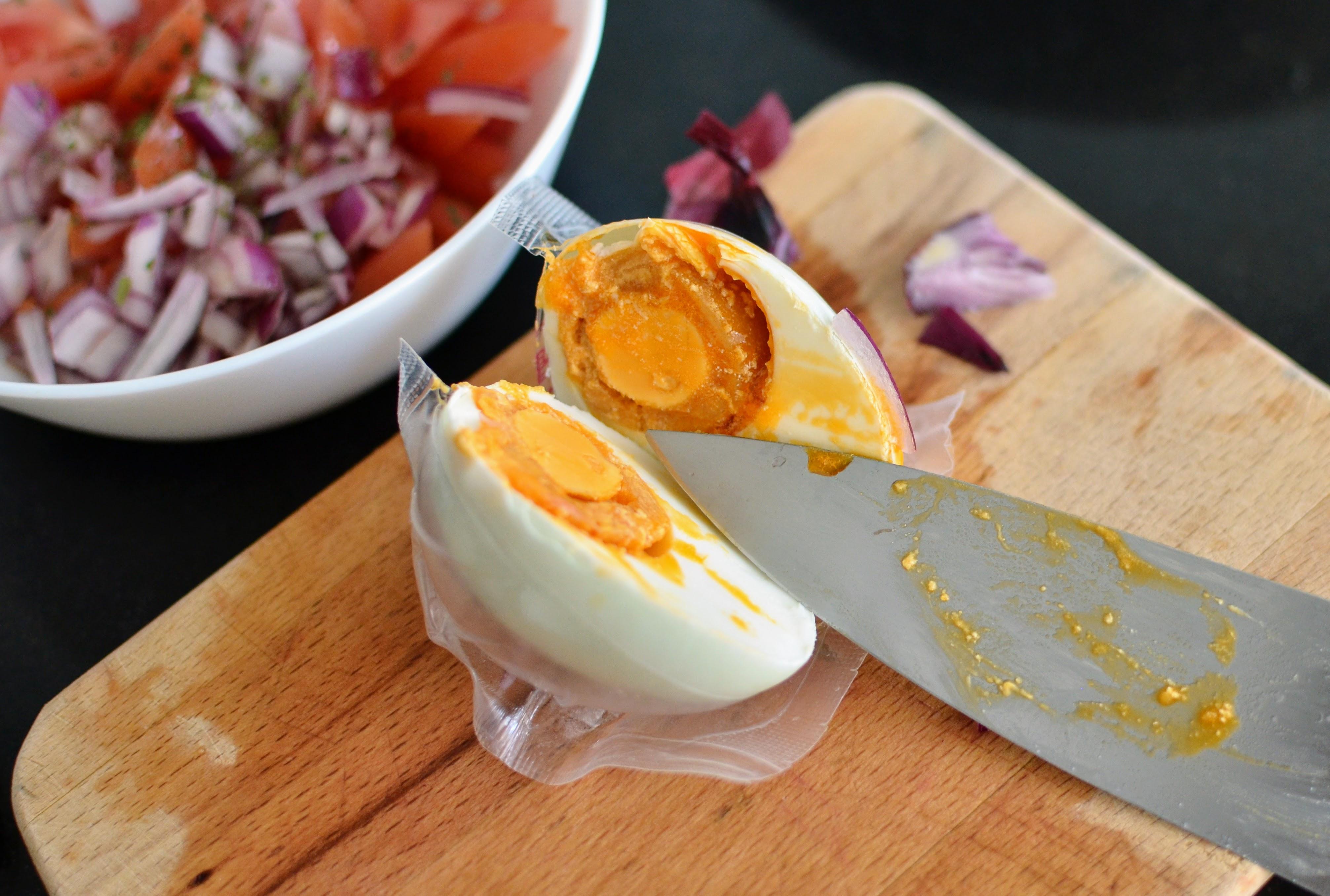A halved salted egg on a cutting board with fresh tomato and onion salad