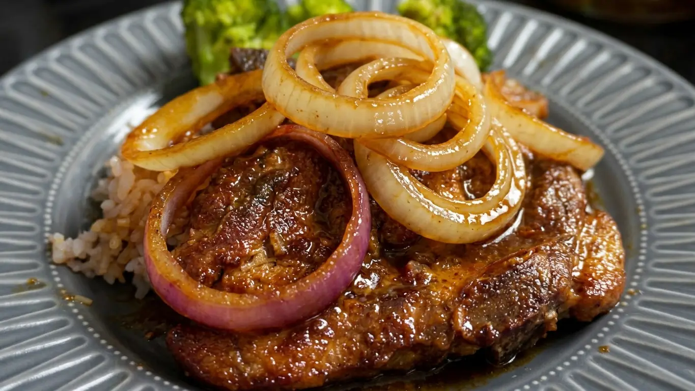 Pork bistek in a glossy soy-calamansi sauce, crowned with sweet onion rings