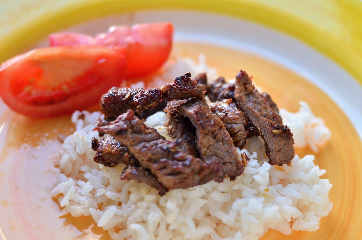 Beef tapa served on a plate with rice and fresh tomato