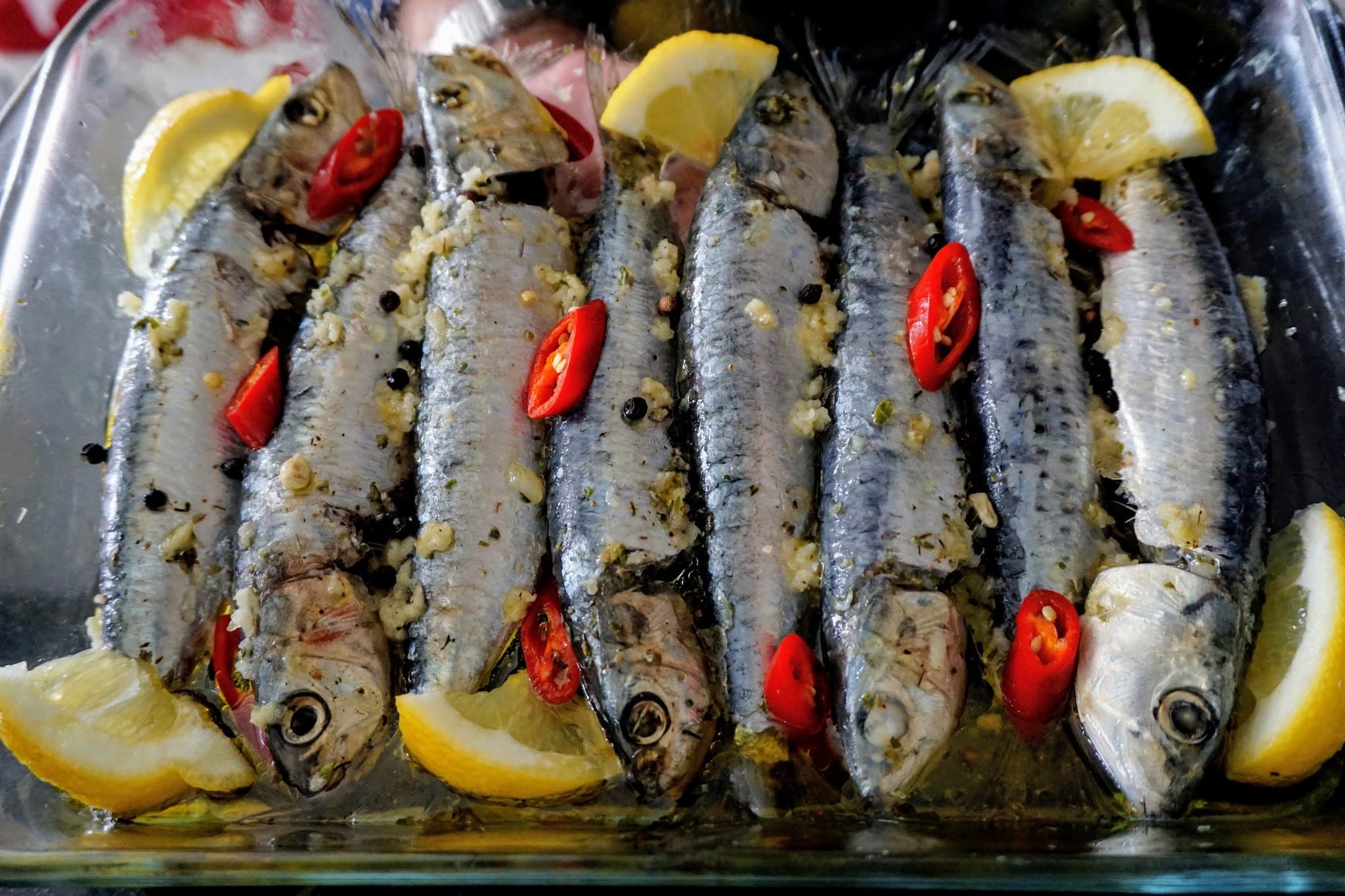 Sardines seasoned with ingredients laying down on a baking glass dish
