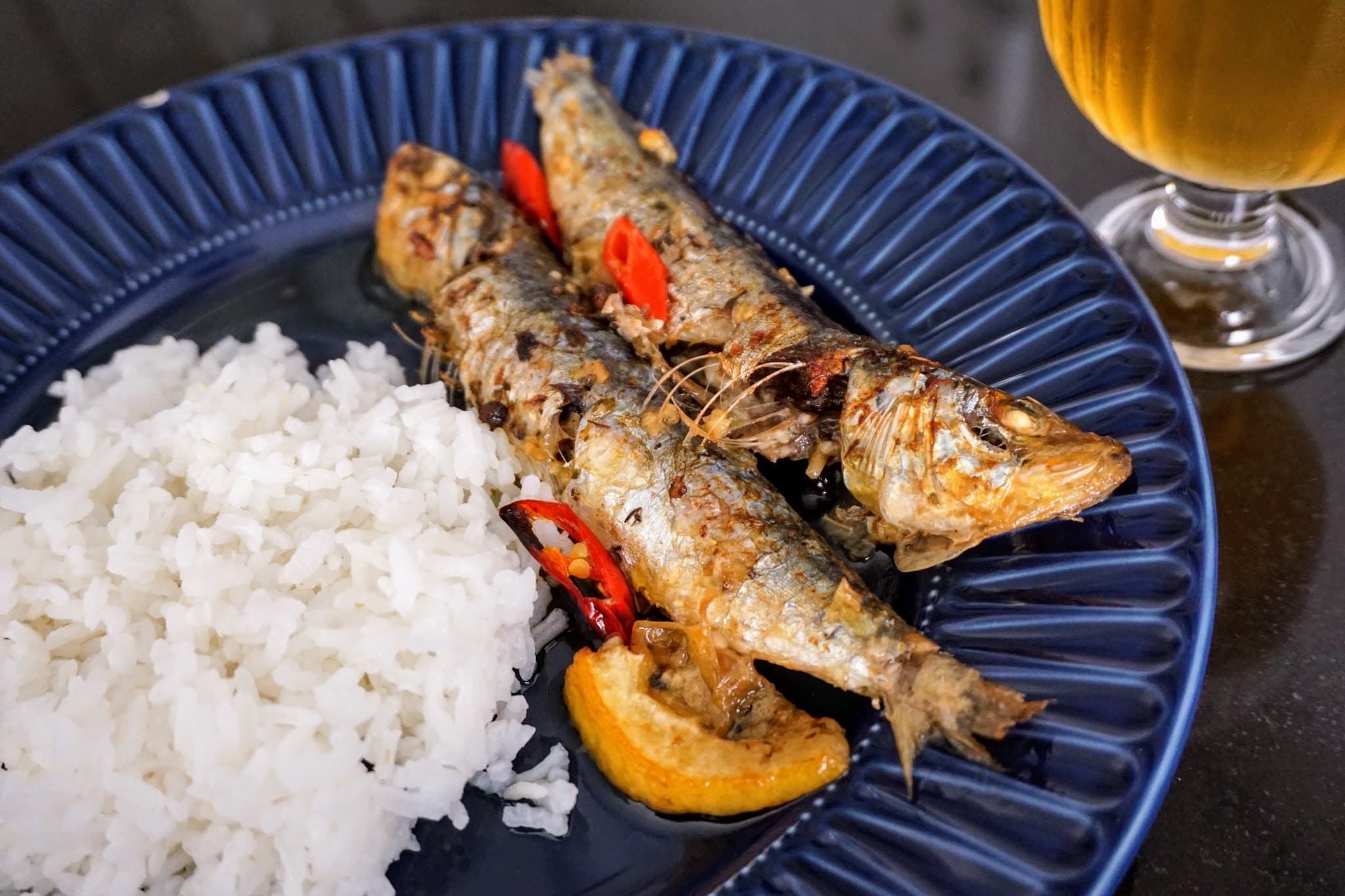 Oven-grilled sardines served on a plate with rice and beer at the side